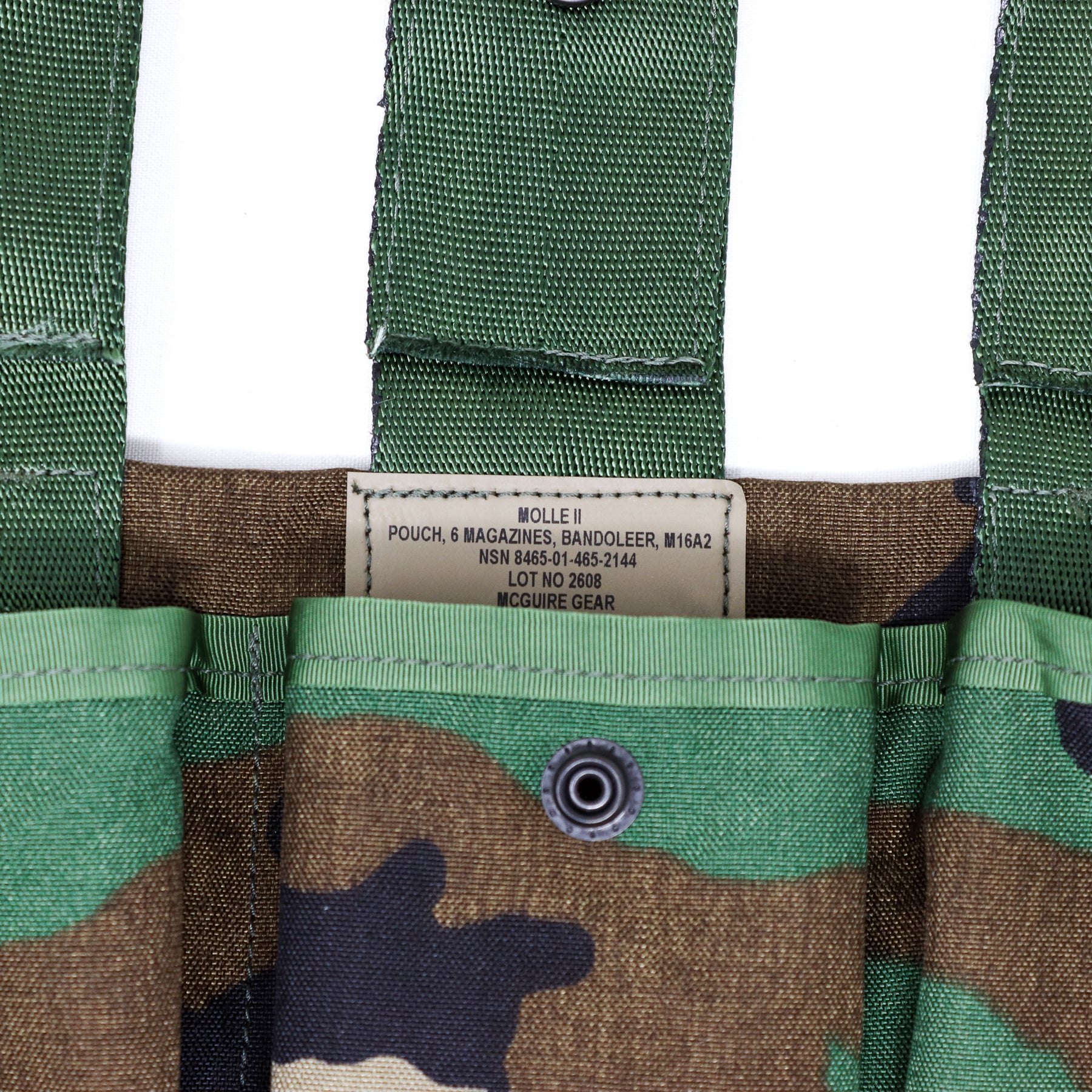 Close-up of a MOLLE II pouch in green, brown, and black camouflage fabric, showing a central label that reads 'MOLLE II POUCH, 6 MAGAZINES, BANDOLEER, W16A2' and 'MOUCURE GEAR'.