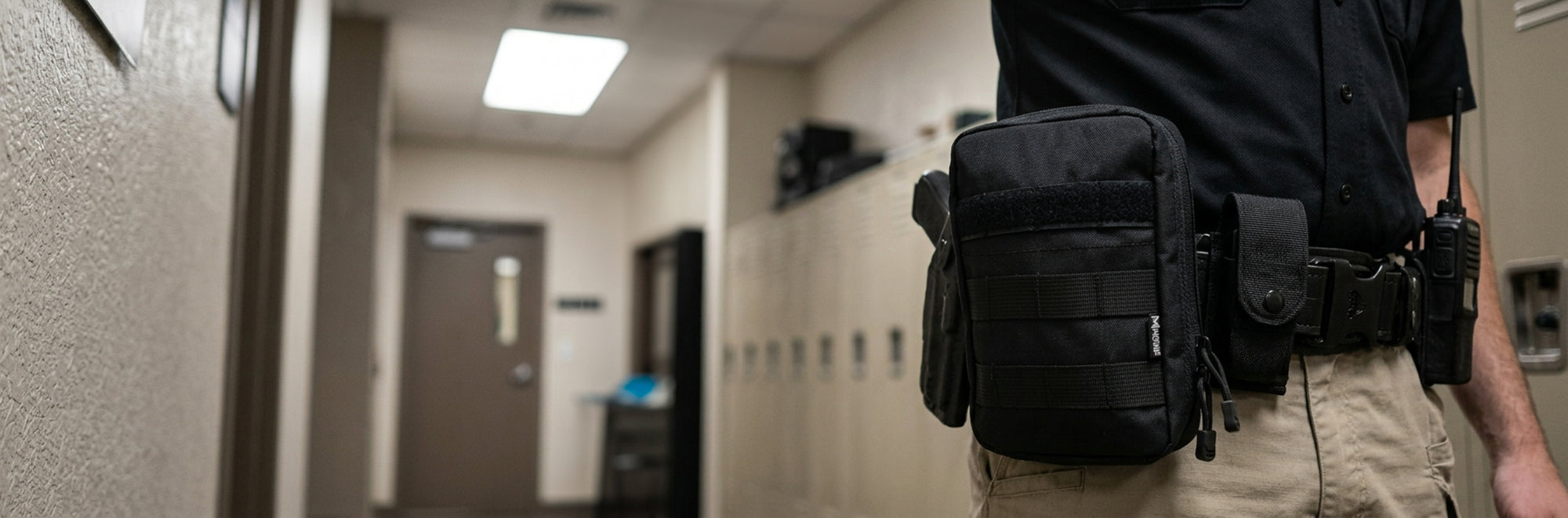 A close-up side view of a person in a uniform wearing a black tactical utility pouch and belt accessories on the right hip, standing in a hallway.